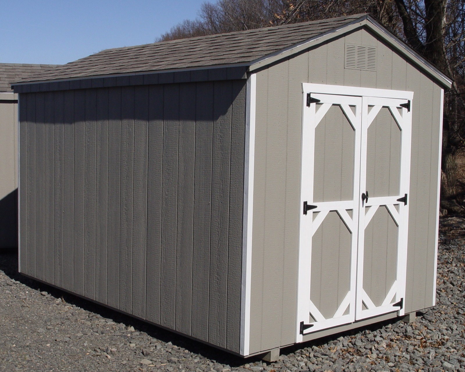 A custom Amish-built wood A-frame storage shed with white trim doors, set on a gravel pad.