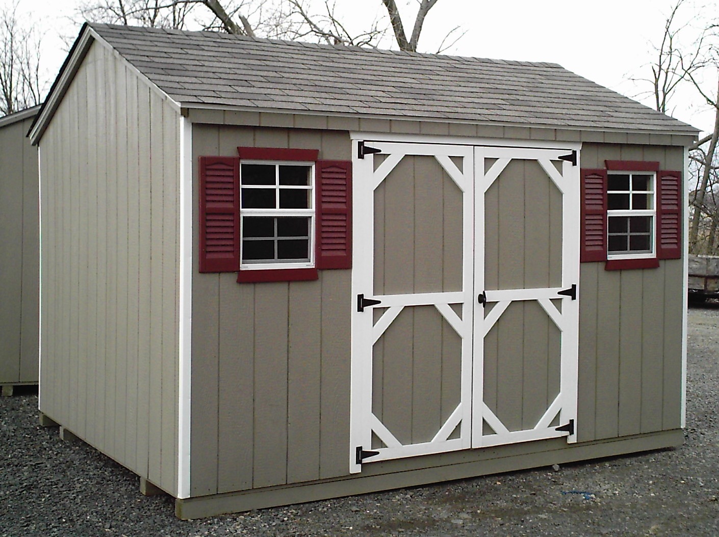 Grey wood A-frame shed with red shutters and double doors.