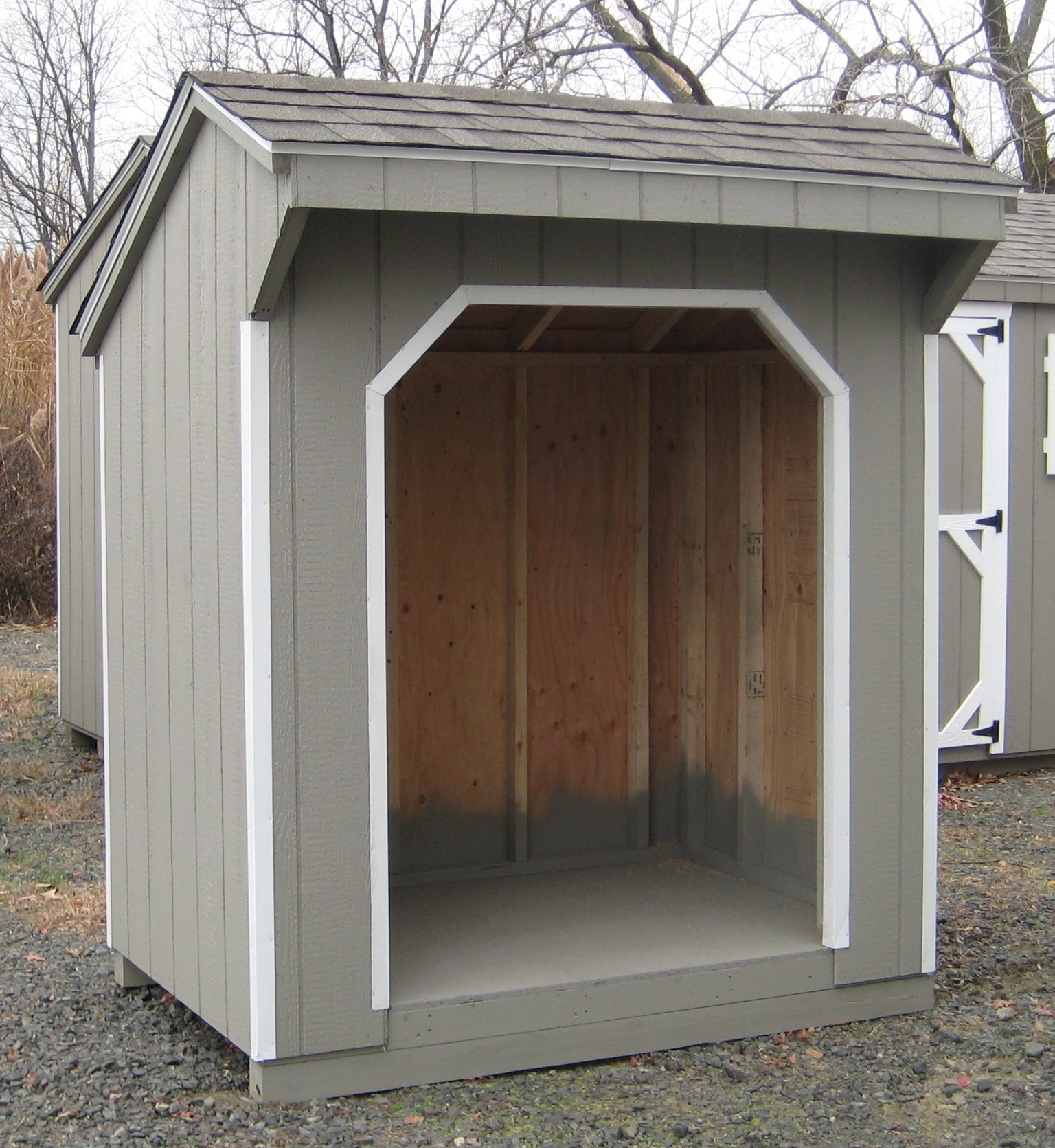 Open-face grey firewood shed with a shingled roof for stacking and seasoning firewood.