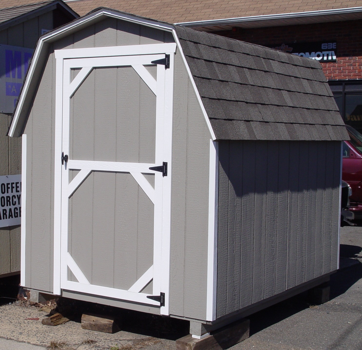Grey Dutch barn style shed with a gambrel roof, used to store a motorcycle.